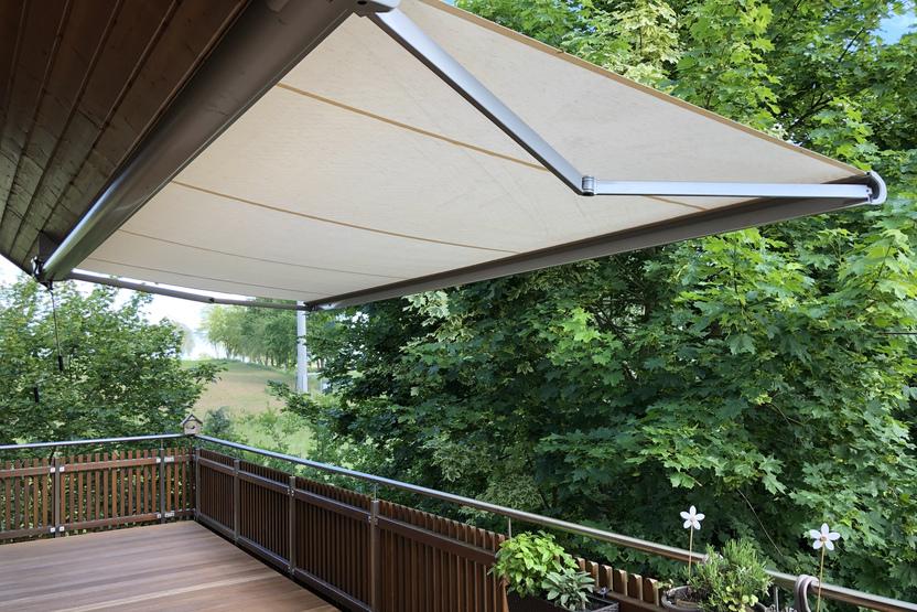 Maßgefertigtes Terrassendeck und Geländer aus Holz, erstellt von einer Bautischlerei, mit einer ausgefahrenen Markise.