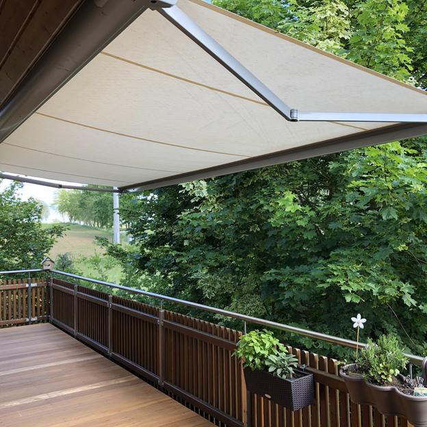 Maßgefertigtes Terrassendeck und Geländer aus Holz, erstellt von einer Bautischlerei, mit einer ausgefahrenen Markise.
