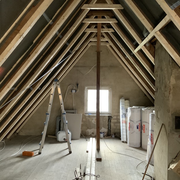 Unfertiger Dachboden im Umbau durch Bautischlerei mit Holzbalken, Dämmmaterial und Werkzeugen.