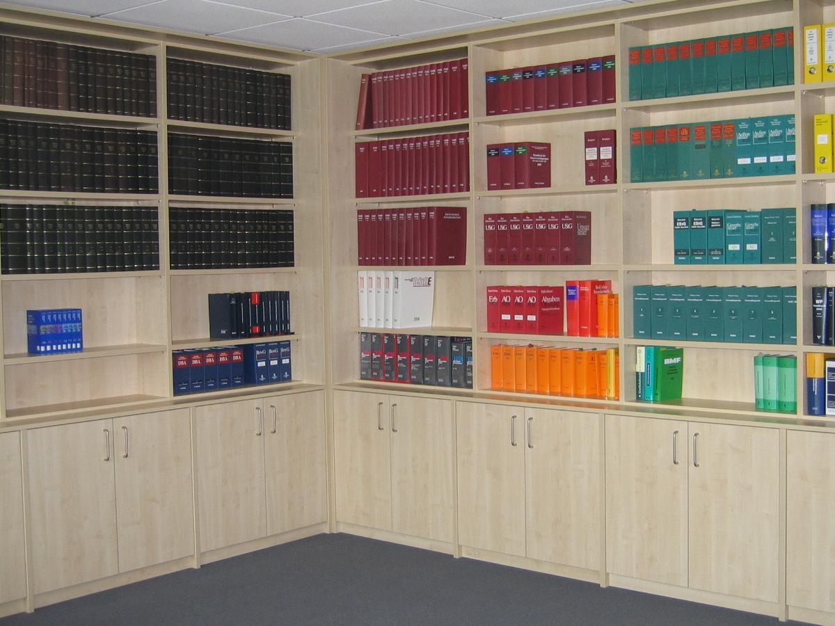 Ein B&uuml;ro mit umfangreichen, hellen B&uuml;rom&ouml;beln nach Ma&szlig;, gef&uuml;llt mit farblich sortierten Ordnern, bietet eine organisierte Arbeitsumgebung.