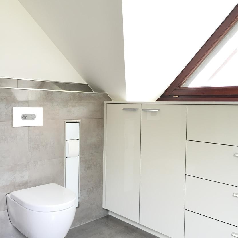 Ein helles, stilvolles Badezimmer unter einem Dachfenster, mit einer schwebenden Toilette und einer großen weißen Schrankwand.