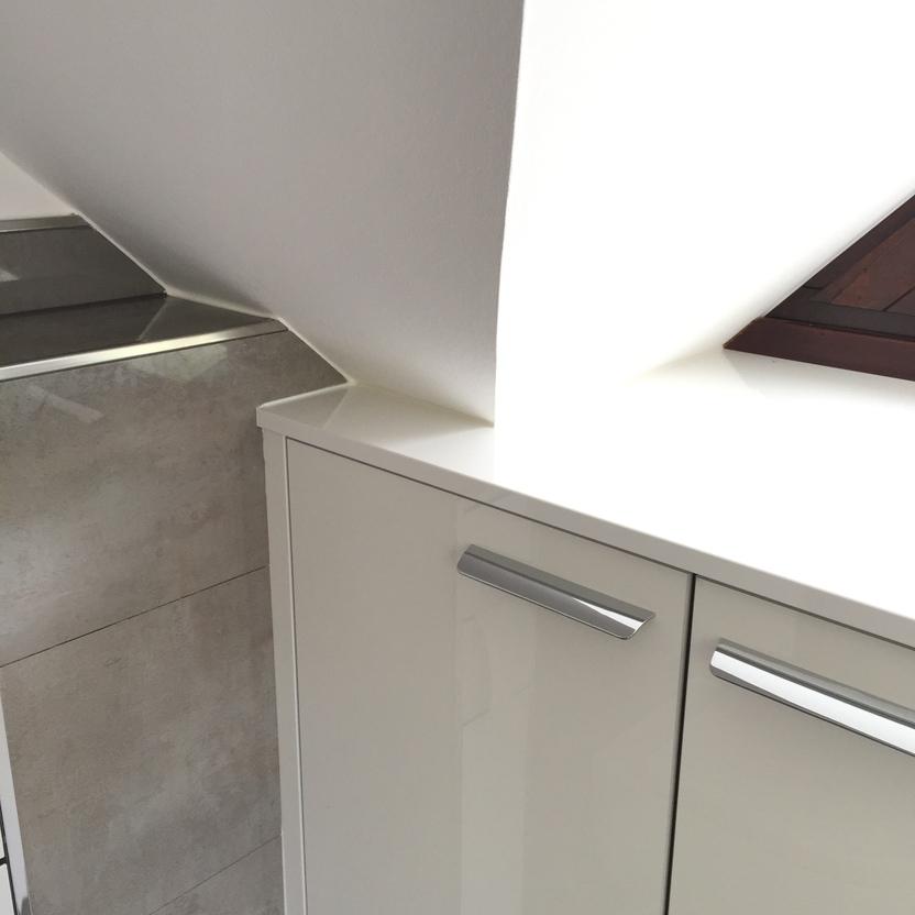 Nahaufnahme eines weißen Badezimmerschranks mit metallenen Griffen, eingepasst unter eine Dachschräge. Ideale Badmöbel nach Maß.