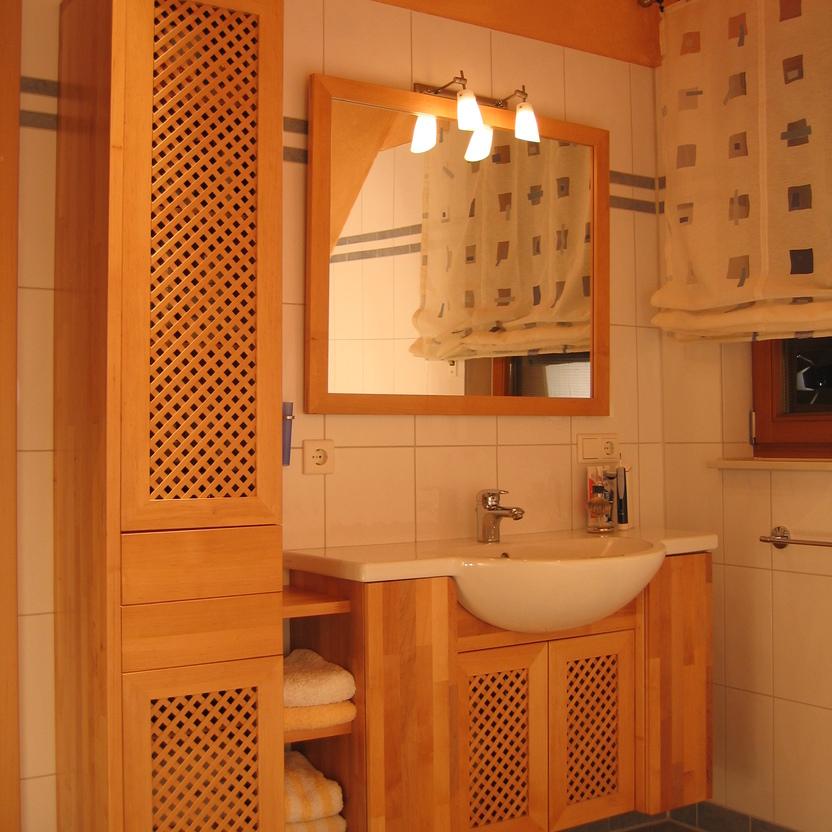 Wohlgestaltetes Badezimmer mit Badmöbeln nach Maß aus Holz, inklusive eines Waschtisches und eines hohen Schrankes mit Gittertüren.
