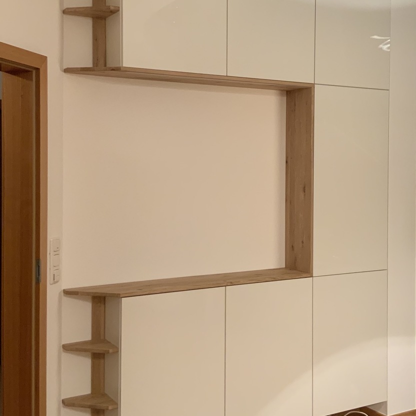 Ein eleganter Schrank nach Maß, der weiße Schranktüren mit offenen Holzelementen und Regalen kombiniert, bietet eine moderne und funktionale Lösung für Stauraum und Dekoration.