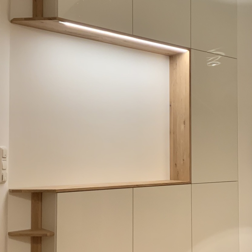 Ein eleganter Schrank nach Maß mit weißen Fronten und offenen Holzelementen. Eine integrierte LED-Leiste sorgt für dezente Beleuchtung, während Regale zusätzlichen Stauraum bieten.