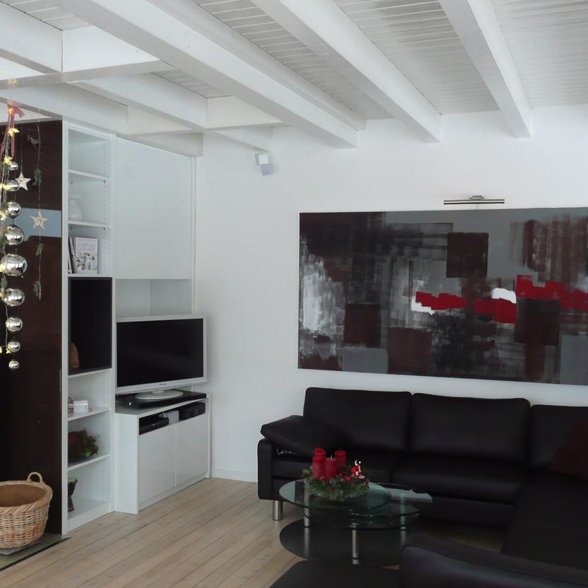 Ein stilvolles Wohnzimmer mit einem Schrank nach Maß, der Fernseher und Regale integriert. Der Kamin ist festlich dekoriert und das Ambiente wird durch moderne Kunst und ein Ledersofa ergänzt.