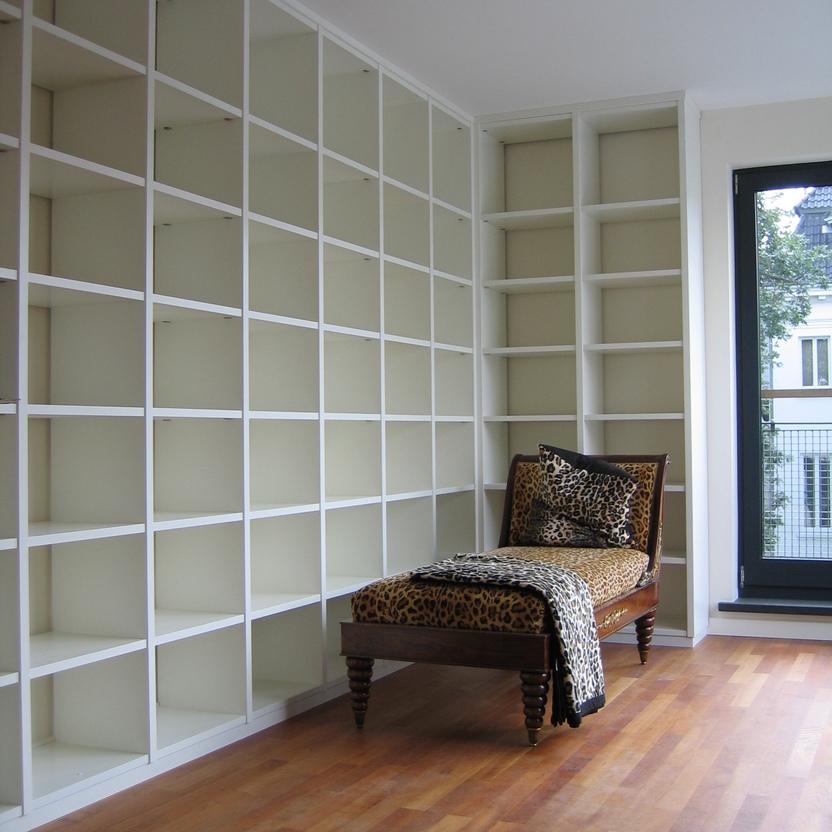 Ein großzügiges Regal nach Maß füllt eine ganze Wand in einem modernen Wohnzimmer. Eine stilvolle Chaiselongue mit Leopardenmuster setzt einen eleganten Akzent im Raum.