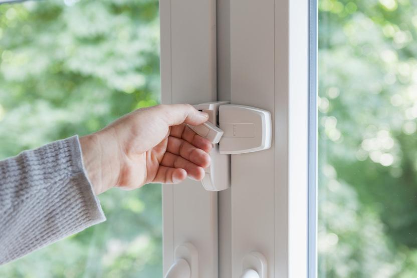 Hand verriegelt ein wei&szlig;es ABUS-Zusatzschloss f&uuml;r mechanischen Einbruchschutz am Fenster.