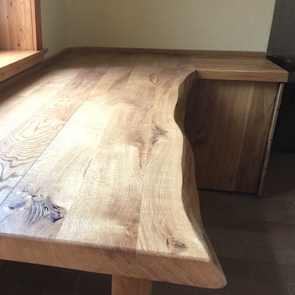 Maßgefertigter Holztisch aus Eiche mit natürlicher Baumkante unter großem Fenster.