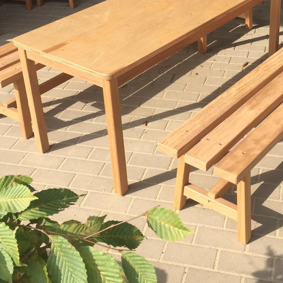 Schlichter Holztisch mit passender Bank aus Massivholz auf gepflasterter Terrasse.