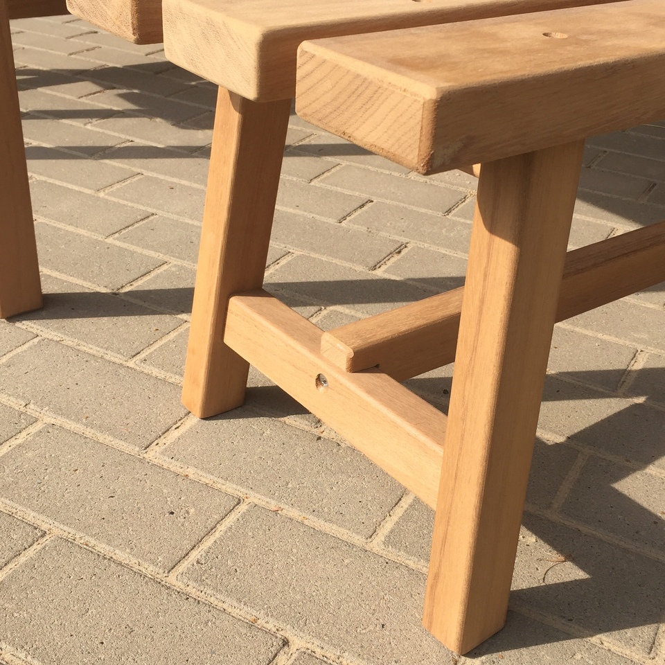 Nahaufnahme einer robusten Gartenbank aus hellem Massivholz auf Steinboden.