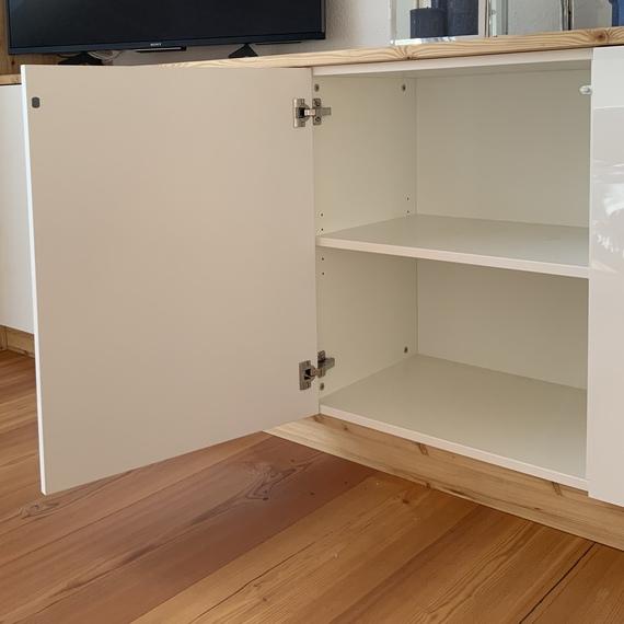 Maßschrank mit offener Tür Weißer Wohnzimmerschrank mit geöffneter Tür und Regalfach, daneben Fernseher auf Holzplatte.