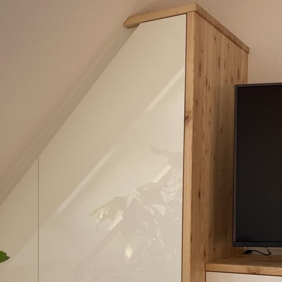 Wei&szlig;er Einbauschrank unter Dachschr&auml;ge neben gro&szlig;em Fenster und gr&uuml;ner Zimmerpflanze.