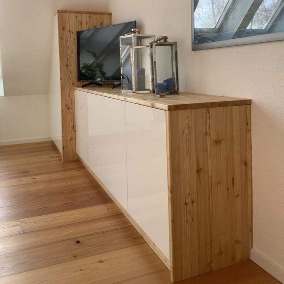 Maßmöbel unter Dachschräge Maßgefertigter Wohnzimmerschrank aus Holz mit weißen Hochglanzfronten und Fernseher.