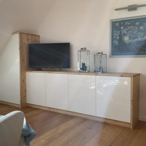 Helles Wohnzimmer mit ma&szlig;gefertigtem TV-Schrank aus Holz und wei&szlig;en Fronten.