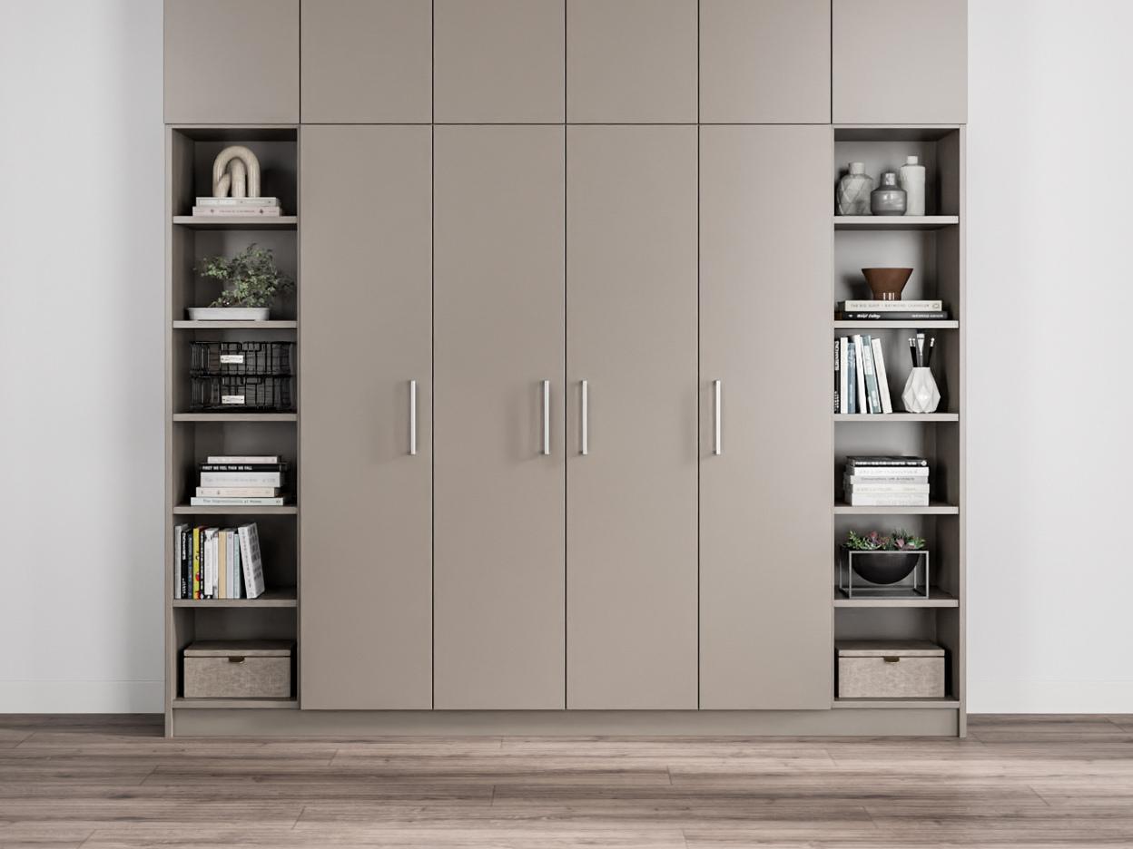 Ein maßgefertigter, taupefarbener Schrank mit glatten Türen, flankiert von offenen Bücherregalen mit diversen Dekorationsobjekten und Aufbewahrungsboxen.